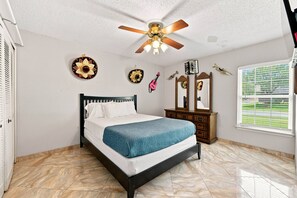 A bedroom with a bed, a ceiling fan, a dresser, and a window with blinds. - Spacious 4BR Retreat Near Lackland AFB & SeaWorld (San Antonio)