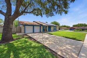 A residential house with a garage, a front yard, and a large tree. - Spacious 4BR Retreat Near Lackland AFB & SeaWorld (San Antonio)