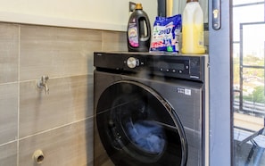 Eine Waschmaschine mit Frontöffnung, mit Waschmittelflaschen und einer Waschnachfüllung auf der Oberseite.