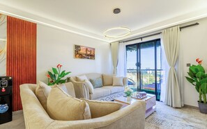 A modern living room with a sofa, a coffee table, and a view of a cityscape through large windows. - Beautiful 2-BR Riara 1 apartment near junction mall with fitness room in Nairobi (Nairobi)