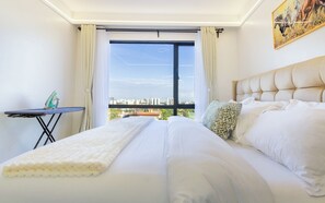 A hotel room with a bed, a table with an iron, and a city view through the window. - Beautiful 2-BR Riara 1 apartment near junction mall with fitness room in Nairobi (Nairobi)