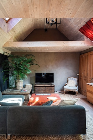 Ein Wohnzimmer mit hohen Decken, einem Fernseher, Sitzgelegenheiten und einer großen Pflanze.