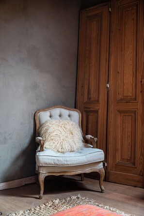 A vintage armchair with a fluffy pillow against a textured wall, next to a wooden wardrobe. - Fleur de Jasmin | A Unique Wellness Retreat near Ghent (Sint-Martens-Latem)