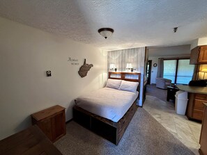 A bedroom with a bed, bedside tables, a small cabinet, a wall-mounted light fixture, and a decorative piece with text. - Pappadeaux's Roost | Cozy Loft with Wood-Burning Fireplace! (Snowshoe)