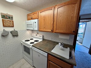 A compact kitchen with white appliances, wooden cabinets, and a tiled backsplash. - Pappadeaux's Roost | Cozy Loft with Wood-Burning Fireplace! (Snowshoe)