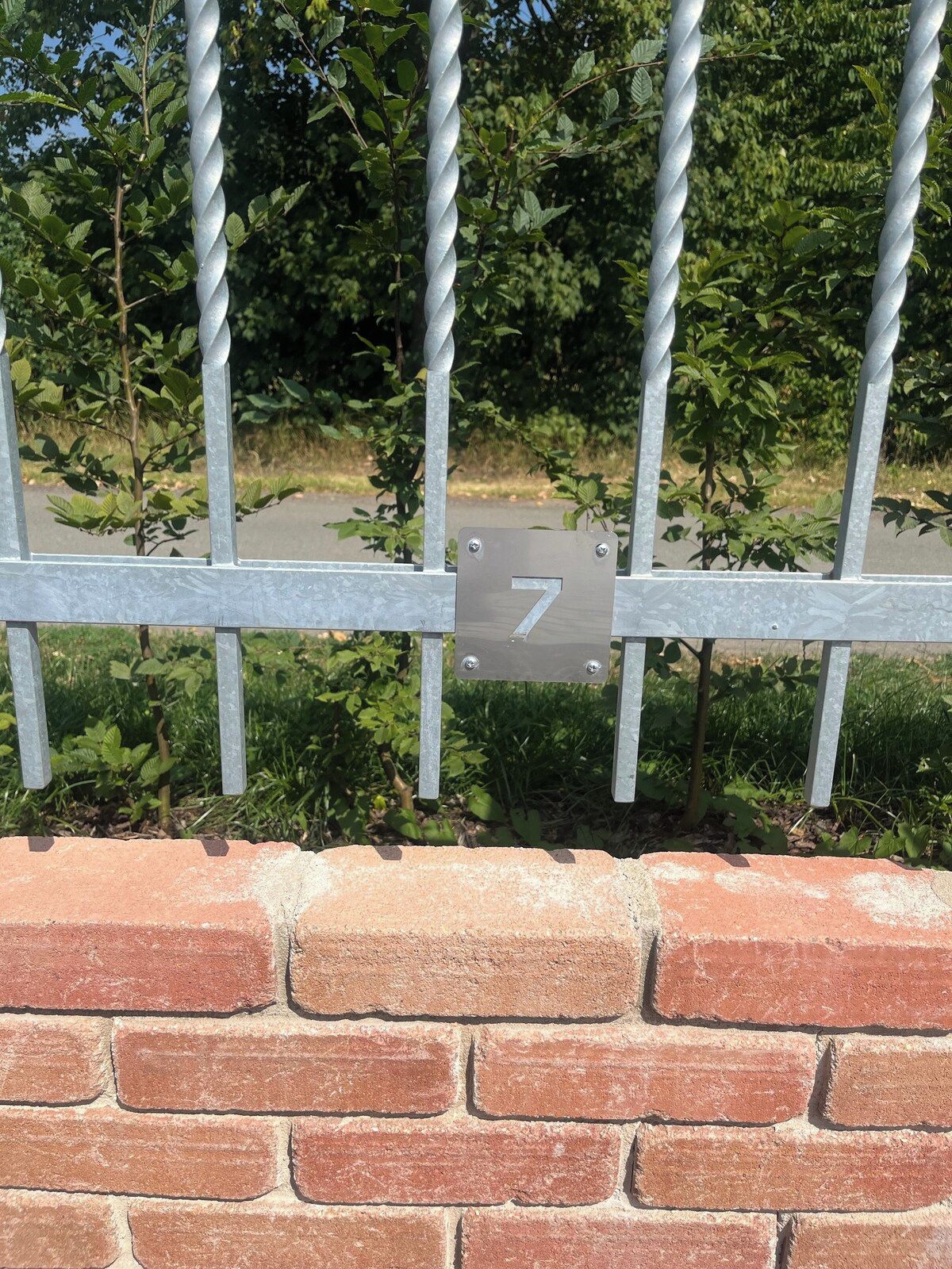 A metal gate with a number sign, a brick wall, and green foliage in the background.