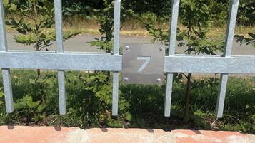 A metal gate with a number sign, a brick wall, and green foliage in the background.