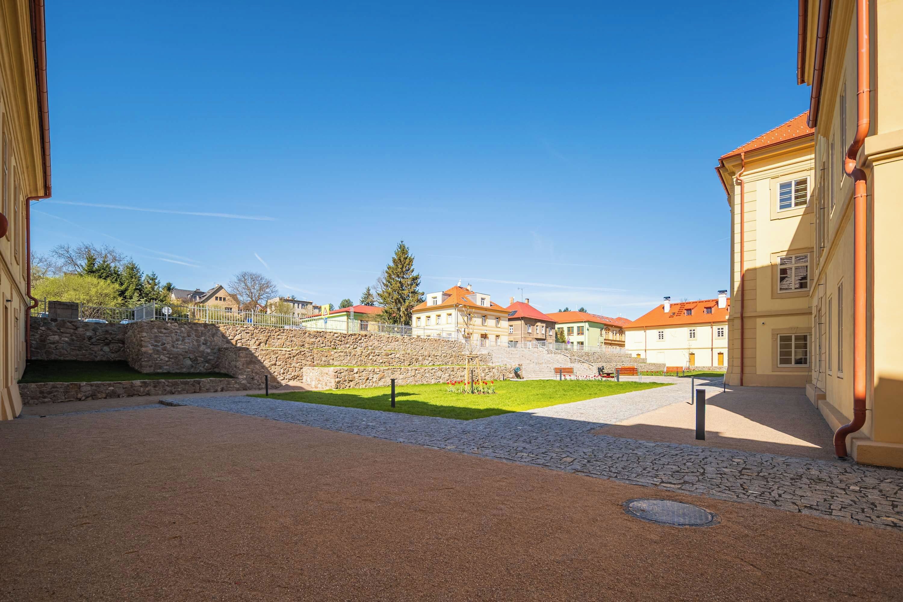 A courtyard with stone walls, a paved area, and buildings with red roofs.