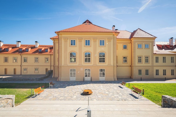 Un edificio ampio e simmetrico con un ingresso centrale, numerose finestre e un cortile pavimentato con panchine.