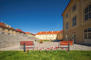 Un cortile con gradini che conducono a un edificio con tetto rosso, panchine e tulipani rossi.