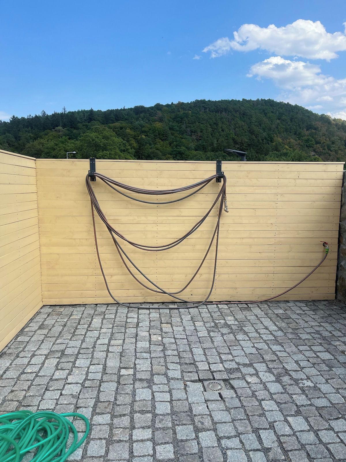 A rooftop terrace with a wooden wall, a metal railing, and a green hose on the ground.