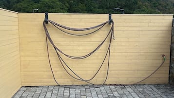 A rooftop terrace with a wooden wall, a metal railing, and a green hose on the ground.