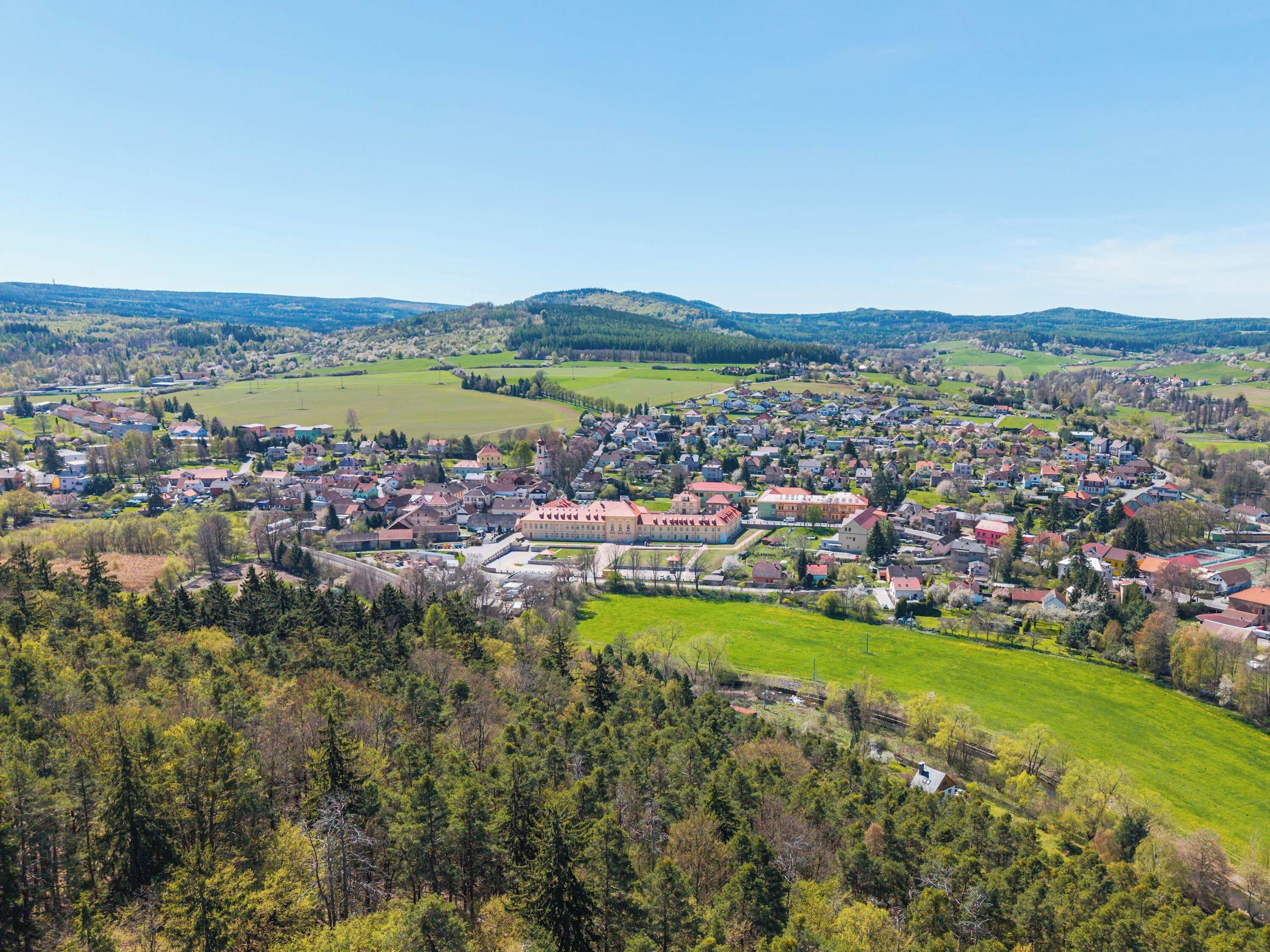 A town with a central square, surrounded by residential buildings and green fields.