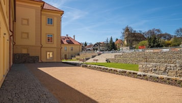 A courtyard with a paved walkway, stone walls, and a building with a red roof.