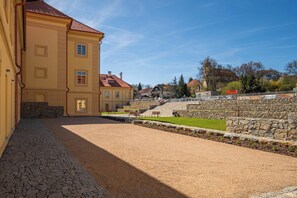 A courtyard with a paved walkway, stone walls, and a building with a red roof. - Historic Jince Castle Stay - Modern Apt & Garden (Příbram)