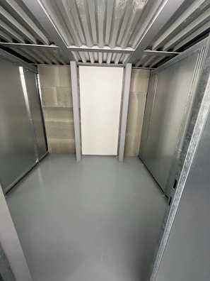 Interno di un ascensore in metallo con una porta bianca e un pavimento grigio.