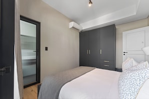 Quarto com cama, guarda-roupa e porta com painel de vidro jateado.