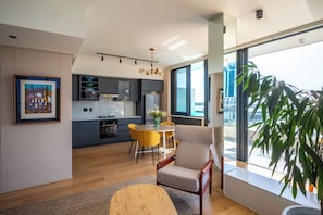 Ein stilvolles Wohnzimmer mit Essbereich, Küche und großen Fenstern mit Blick auf die Stadt.