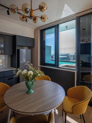 A modern kitchen with a built-in refrigerator, a dining area with a round table and yellow chairs, and a large window offering a view of a swimming pool and buildings. - 2-bedroom Penthouse in the Waterkant Cape Town (Cape Town)