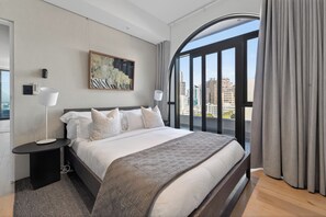 A modern hotel room with a large bed, a city view, a painting on the wall, and a window with curtains. - 2-bedroom Penthouse in the Waterkant Cape Town (Cape Town)