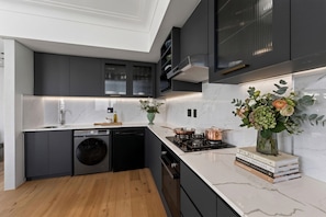 Cozinha moderna com armários escuros, máquina de lavar louça embutida, fogão e pia.