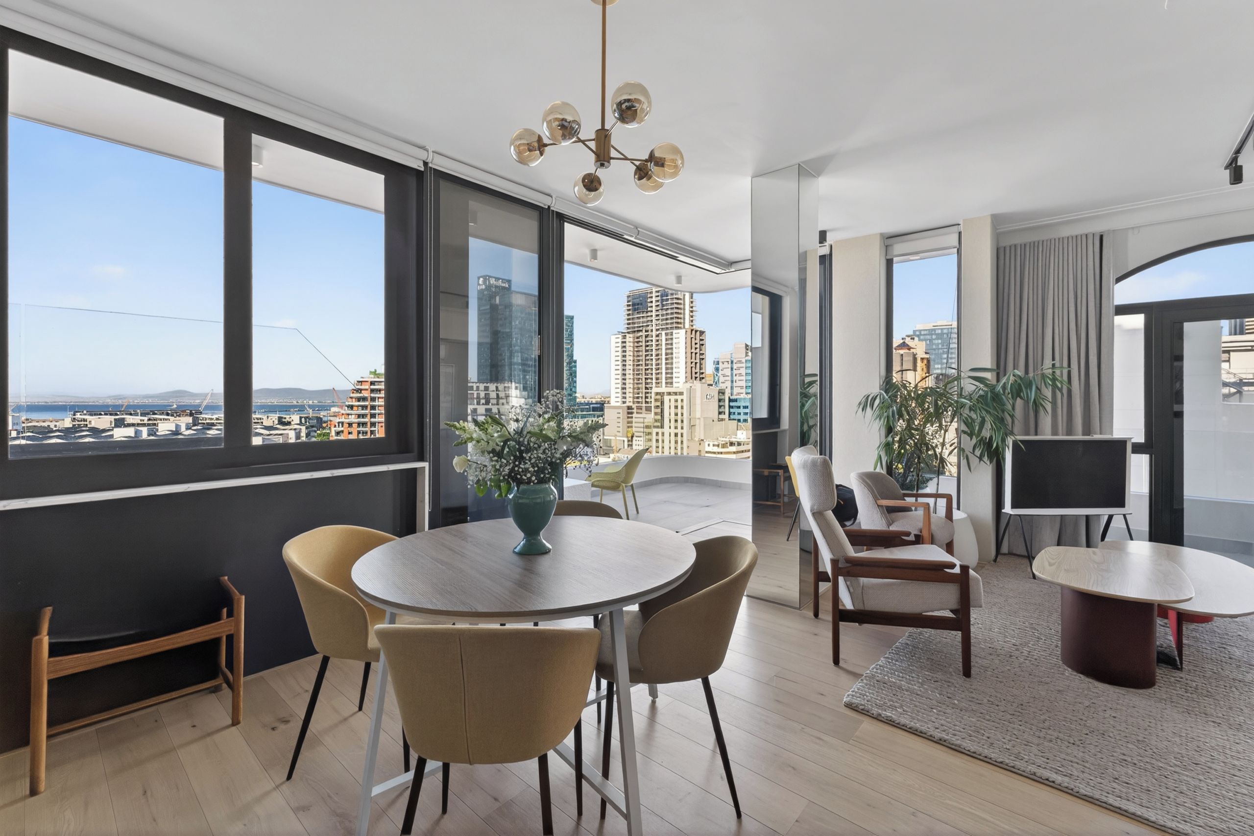 A modern living room with a large window, a dining table, and chairs.