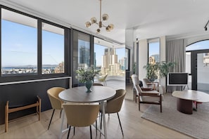A modern living room with a large window, a dining table, and chairs. - 2-bedroom Penthouse in the Waterkant Cape Town (Cape Town)