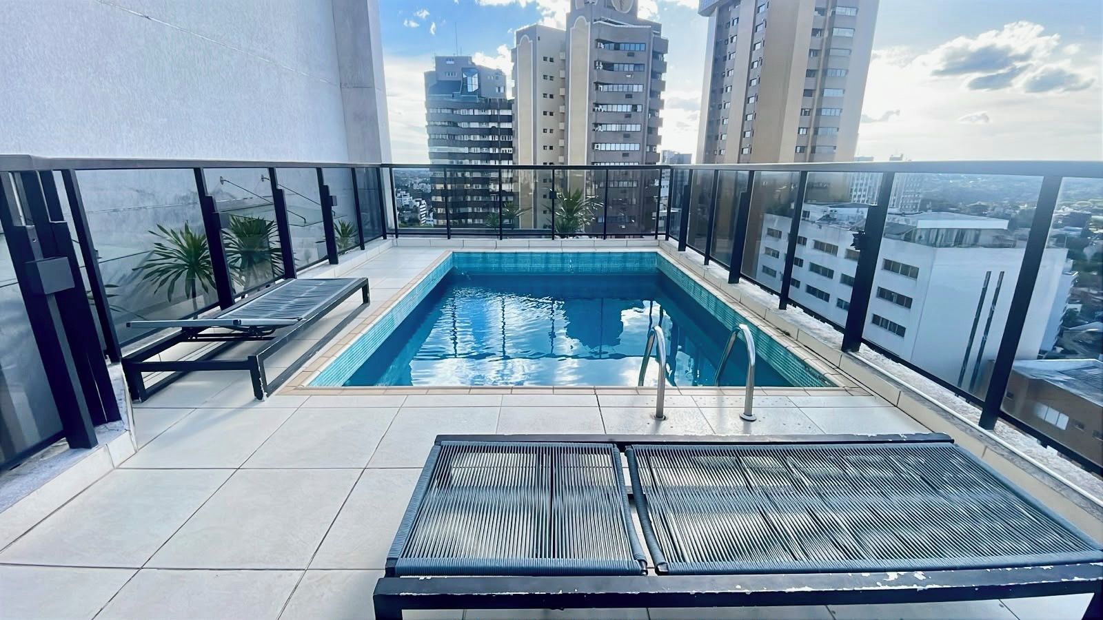 Une piscine sur le toit offrant une vue sur les bâtiments environnants, un espace de détente avec des chaises longues et une rambarde en métal.
