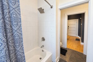 A bathroom with a bathtub, a showerhead, and a door leading to another room.