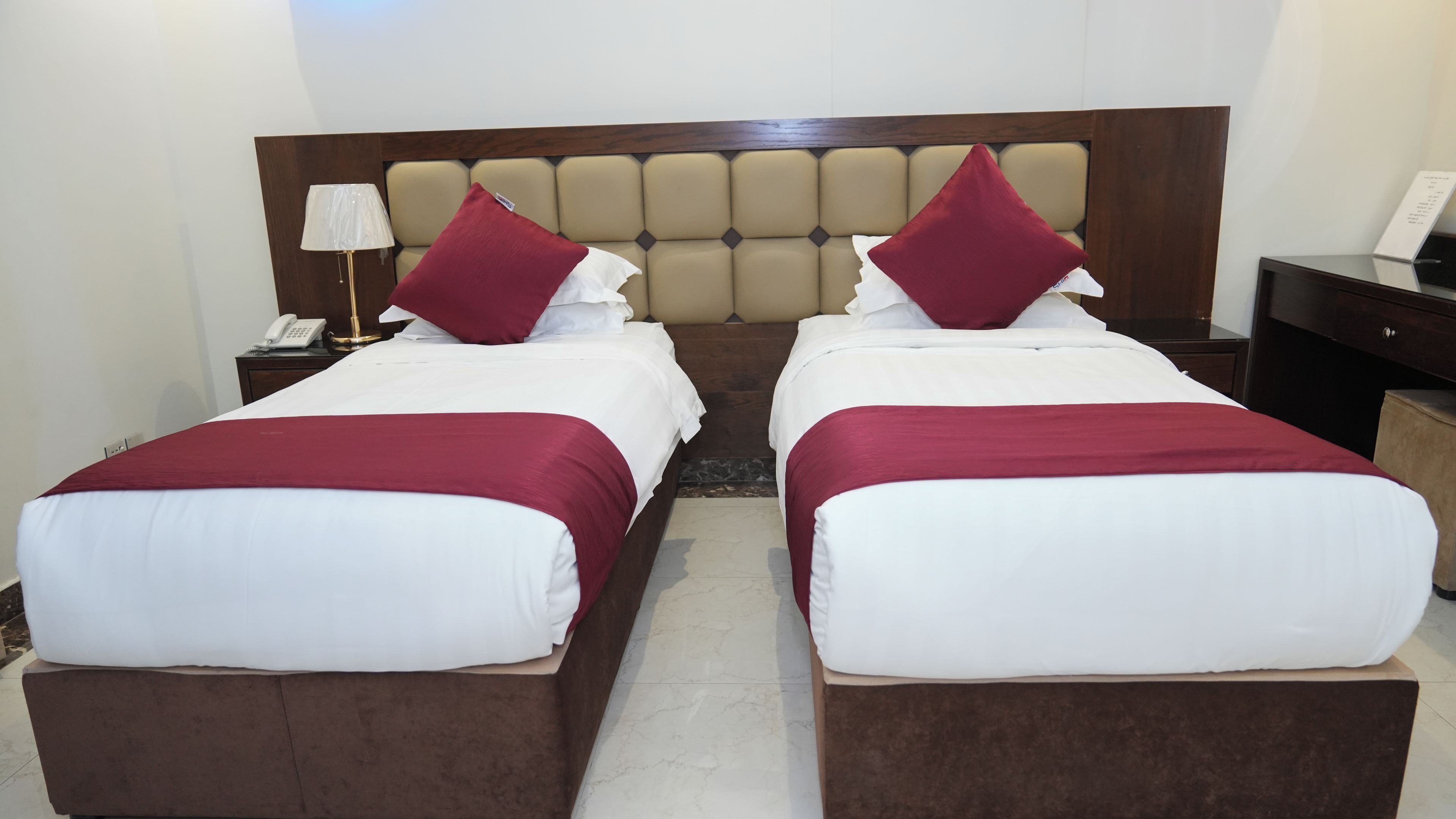 A double room with two beds, a wooden headboard, a nightstand with a lamp, and a small table with a phone.