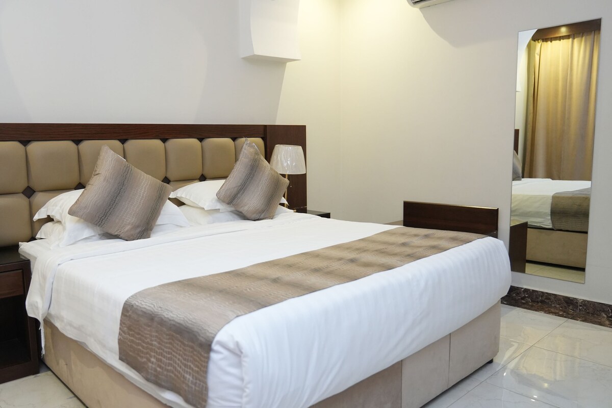 Une chambre d’hôtel avec un lit, une table de chevet, une lampe et un miroir.