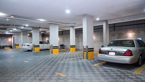 Un parking à plusieurs niveaux avec des voitures garées, des piliers en béton et un éclairage au plafond.