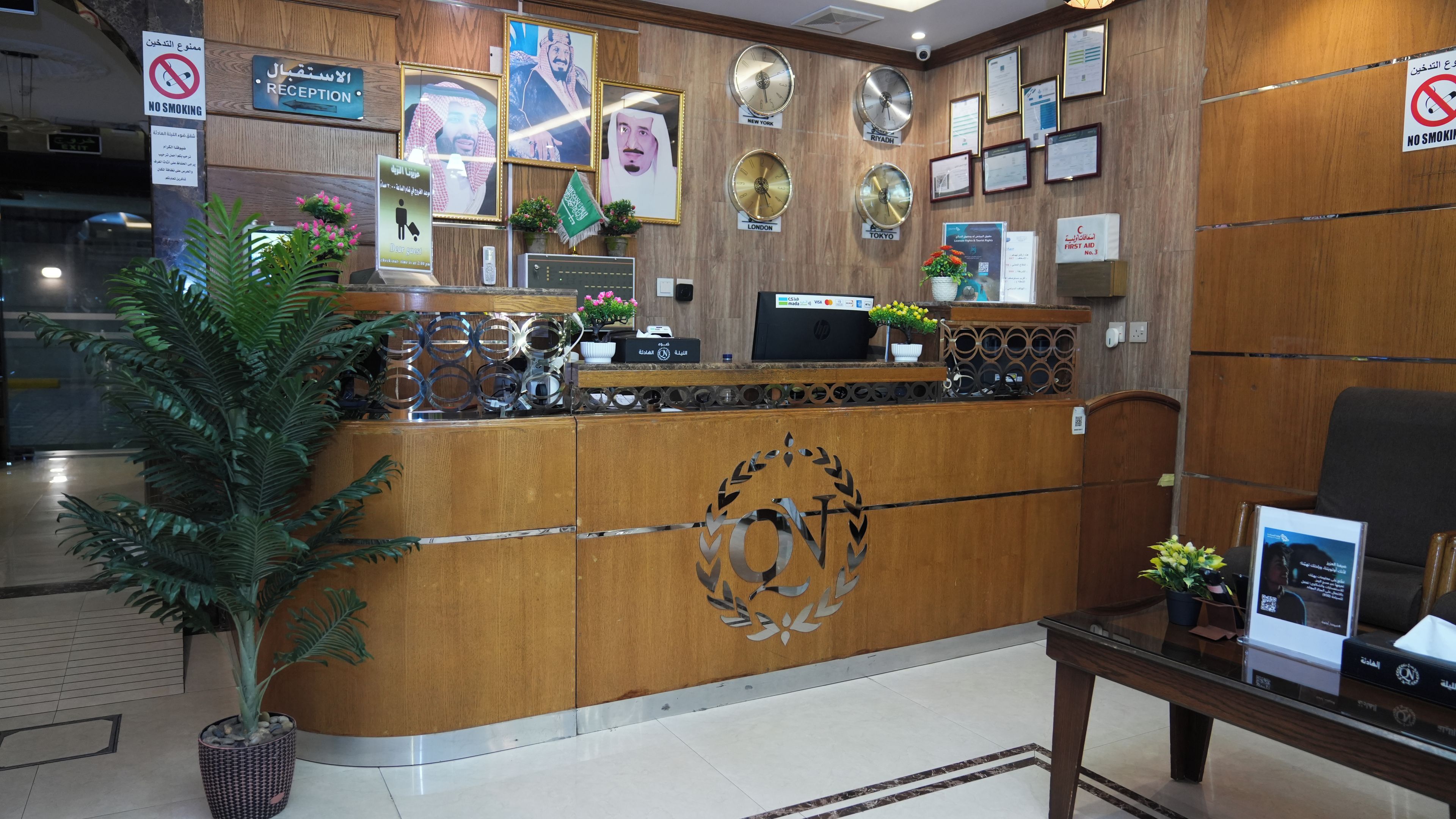 A reception desk with a wooden finish, a digital screen, and a wall adorned with clocks and framed certificates.