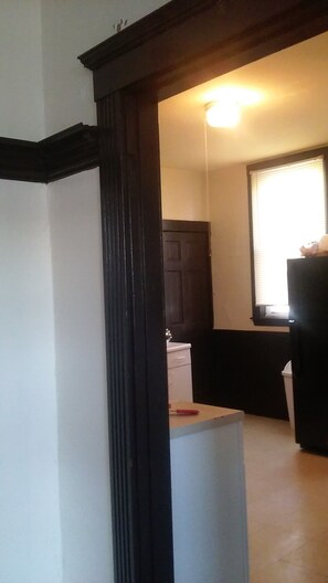 A hallway leading to a kitchen with a white refrigerator, a wooden cabinet, and a window with blinds. - Beautiful 3-bedroom apartment with AC in vibrant Boston (Boston)