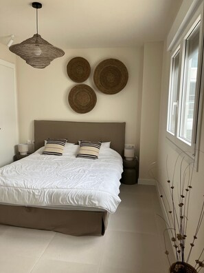 A bedroom with a large bed, a hanging light fixture, and wall decor. - New Listing (Estepona)