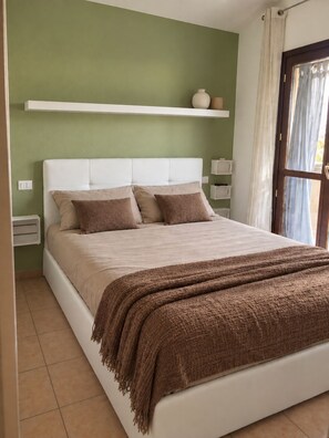 A bed with a white headboard, beige bedding, and a brown throw blanket. - New Listing (Sardegna)