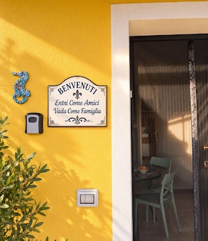 A yellow wall with a welcome sign, a doorbell, and a light switch. - New Listing (Sardegna)