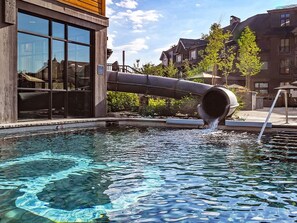 A swimming pool with a large pipe discharging water into it, surrounded by buildings and trees. - Grand Colorado on Peak 8, 1-Bedroom Condo Steps from Ski Lifts (Breckenridge)