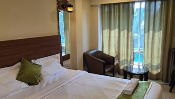 Habitación de hotel con una cama grande, un escritorio, una silla, un ventilador de techo y una ventana con cortinas.