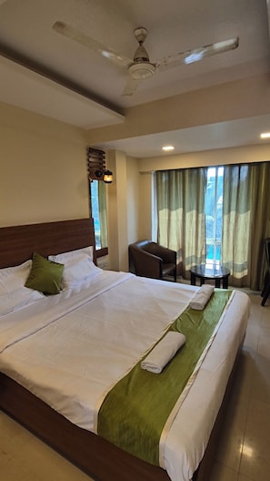 Habitación de hotel con una cama grande, un escritorio, una silla, un ventilador de techo y una ventana con cortinas.