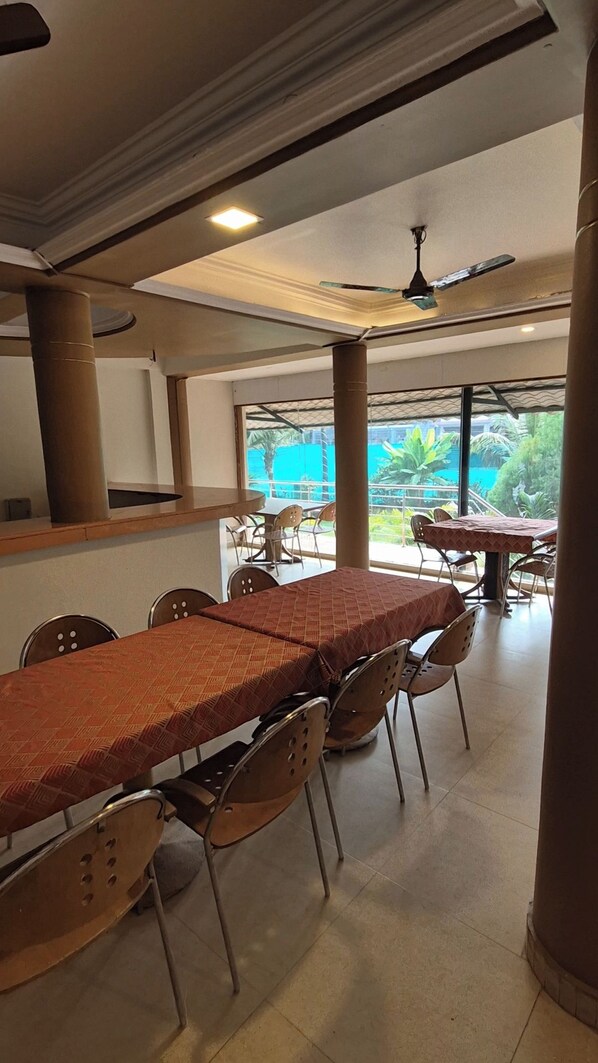 A dining area with a long table and chairs, a ceiling fan, and a view of greenery outside.