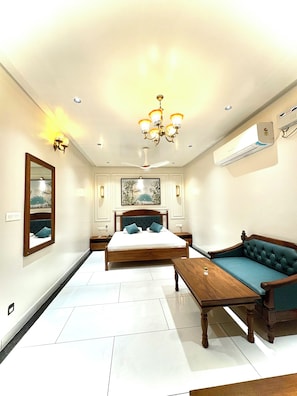 A bedroom with a bed, a sofa, a wooden table, a mirror, and a ceiling fan.