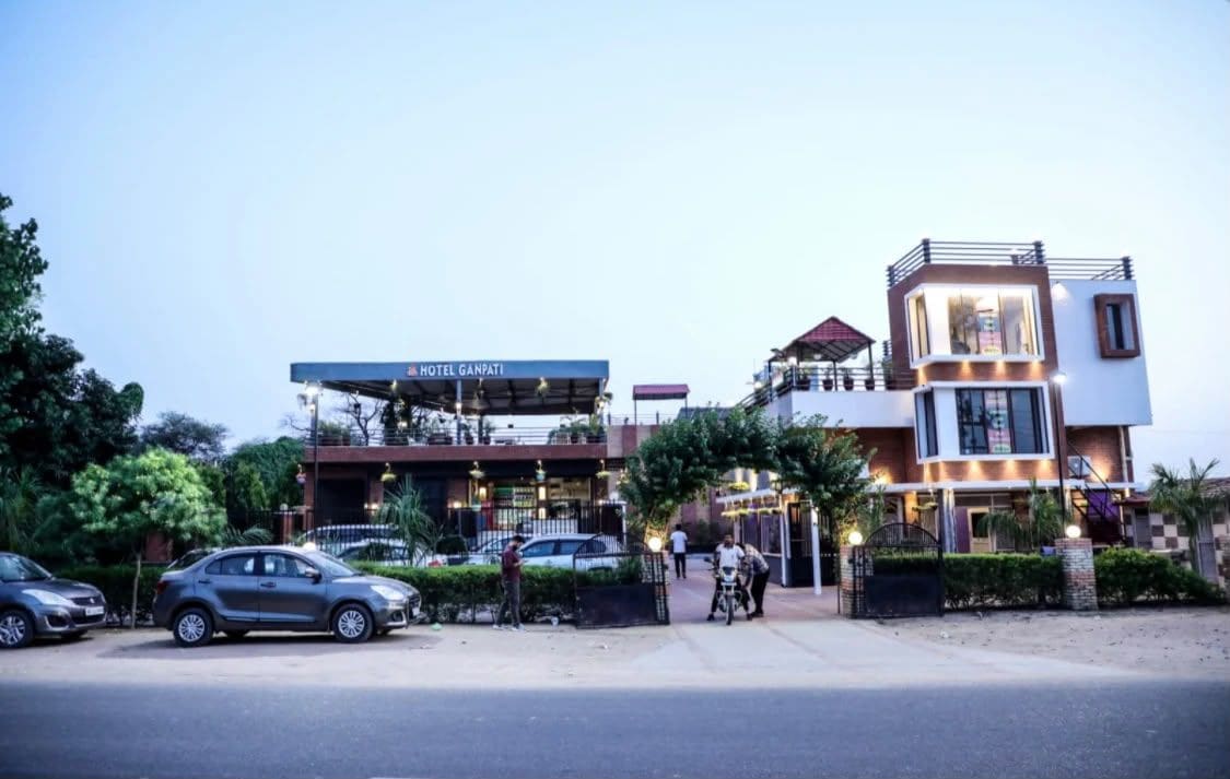A hotel with a signboard, a gated entrance, and parked cars.