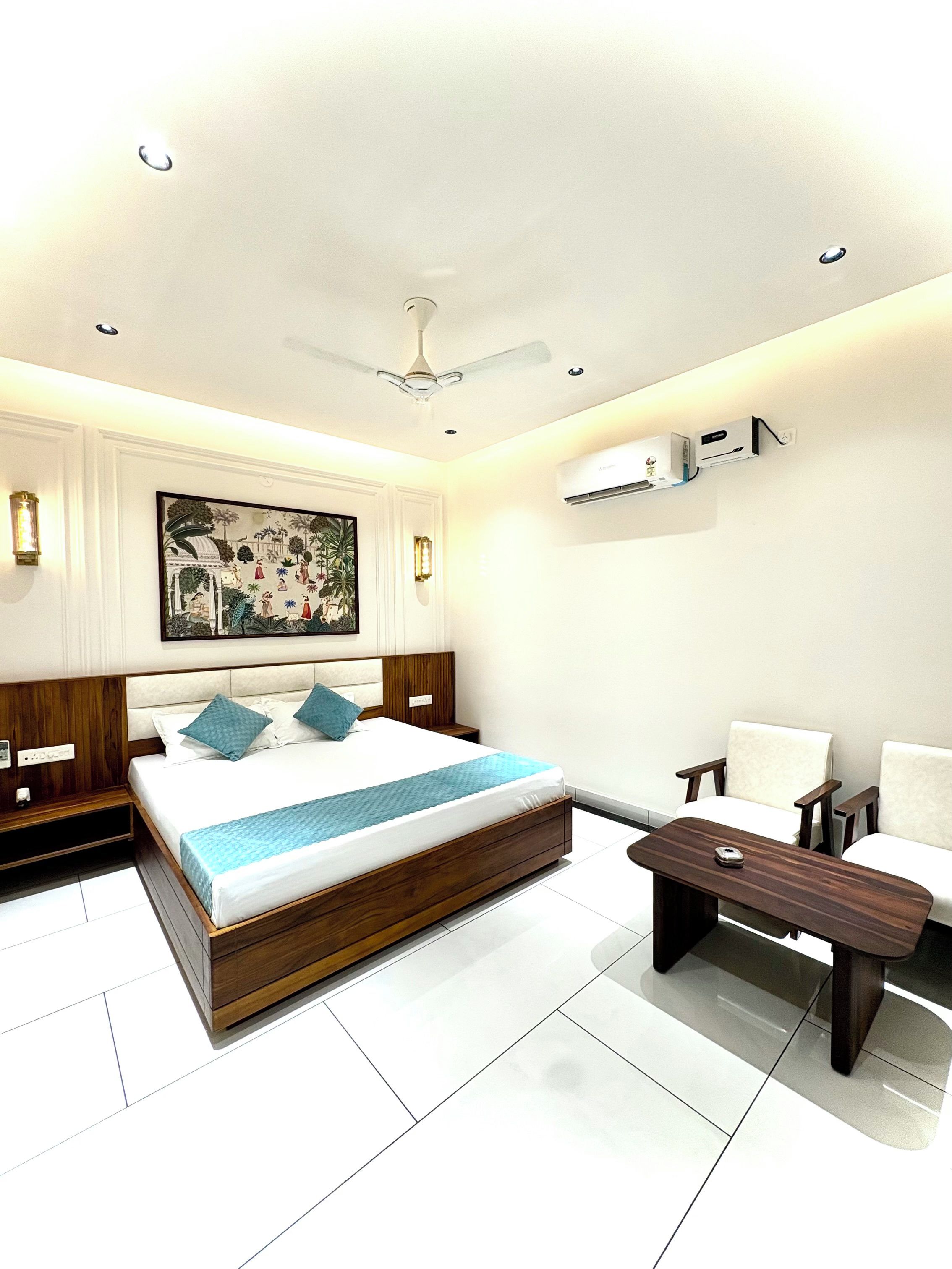 A modern bedroom with a bed, bedside tables, a desk, chairs, a ceiling fan, and an air conditioning unit.