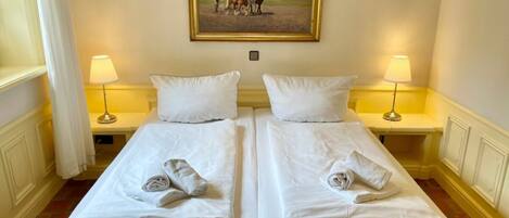 Una habitación de hotel con dos camas individuales, ropa de cama blanca, un cuadro de caballos en la pared y lámparas de noche.