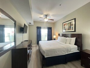 A hotel room with a bed, a ceiling fan, a TV mounted on the wall, and a window with curtains. - 4 BD/ 3 BA/ Villas At Seven Dwarfs Lane (16-108) (Kissimmee)