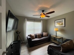 A living room with a ceiling fan, a television, a sofa, a lamp, and a framed picture on the wall. - 4 BD/ 3 BA/ Villas At Seven Dwarfs Lane (16-108) (Kissimmee)