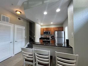 A kitchen with a central island, wooden cabinets, stainless steel appliances, and a white ceiling with recessed lighting. - 4 BD/ 3 BA/ Villas At Seven Dwarfs Lane (16-108) (Kissimmee)