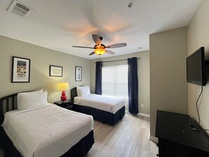 Une chambre d’hôtel avec deux lits, un ventilateur de plafond, une télévision et des tableaux encadrés au mur.