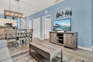 A modern living room with a dining area, a kitchen in the background, and a large flat-screen TV mounted on a wooden cabinet. - Relaxing 3 BD/ 2 BA/ West Lucaya - 3204 GL (Kissimmee)